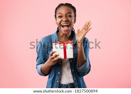 Birthday Gift. Joyful Black Woman Shouting Holding Wrapped Present Box Standing Posing On Pink Background, Looking At Camera. Happy Holiday Celebration Concept. Studio Shot