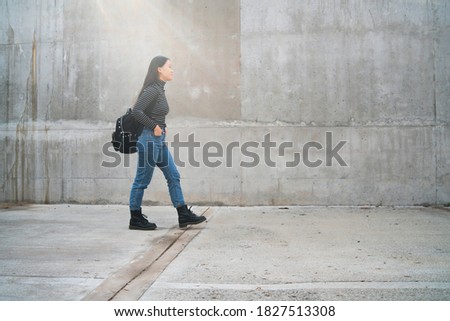 Portrait of young Asian woman walking outdoors against grey wall. Urban concept.
