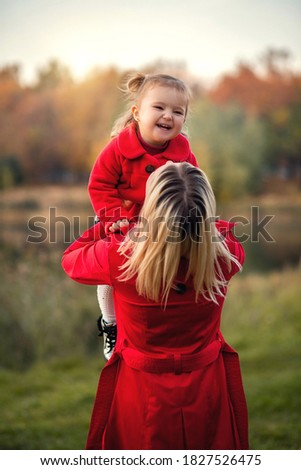 Mom throws her daughter up. The girl smiles. They are wearing red clothes. Autumn photo session.