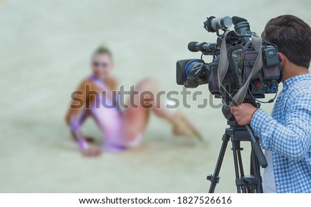 Cameraman shooting live broadcast from gymnastics game to television and internet on the background blured Unidentified women gymnast