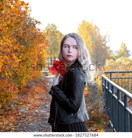 Young woman wearing leather jacket is posing with bright autumn leaves. Enjoying the autumn season