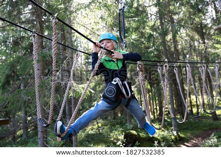 Kid overcoming hanging ropes obstacle in forest adventure park, Karelia