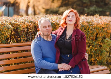 A red-haired woman sits on the lap of a five-year-old man on a park bench in the fall