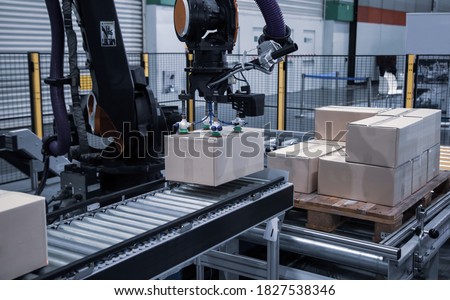 Industrial robot arm loading carton on conveyor in manufacturing production line Royalty-Free Stock Photo #1827538346