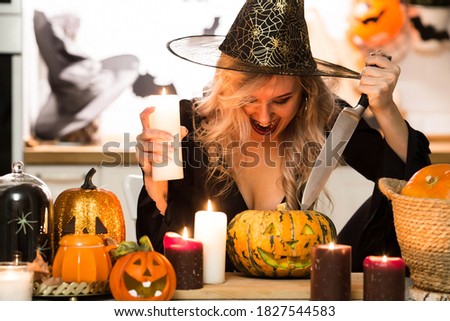 Halloween Witch with pumpkins. Beautiful young woman in a witch costume by candlelight at the table. Halloween decor.