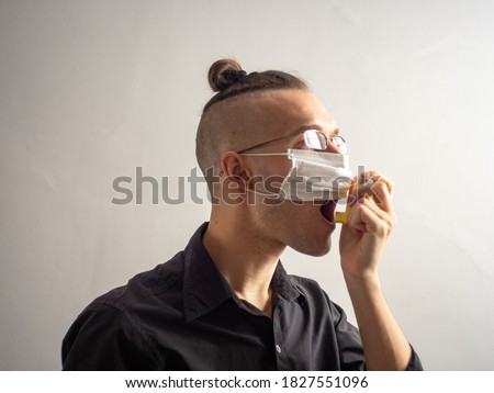 Young Blond Hair Caucasian Male in Black Shirt and Glasses Wears a Disposable Face Mask for Covid-19, Uses Salbutamol Inhalator for Asthma and Allergy Related Breathing Problems Royalty-Free Stock Photo #1827551096