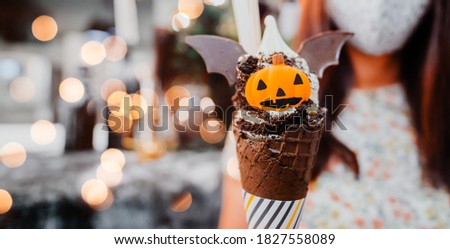 Woman girl holding ice cream cone and Jack o lantern pumpkin on golden bokeh background.sweets for the celebration of Halloween.Halloween party food celebration in holidays.Delicious dessert party.