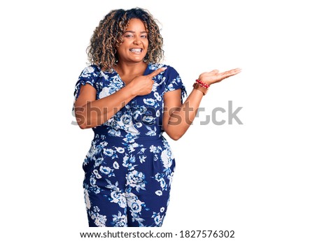 Young african american plus size woman wearing casual clothes amazed and smiling to the camera while presenting with hand and pointing with finger. 