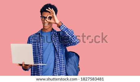 Young african american man holding student backpack using laptop smiling happy doing ok sign with hand on eye looking through fingers 