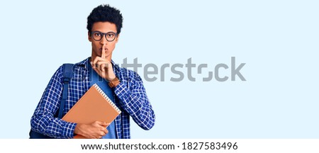 Young african american man wearing student backpack holding book asking to be quiet with finger on lips. silence and secret concept. 