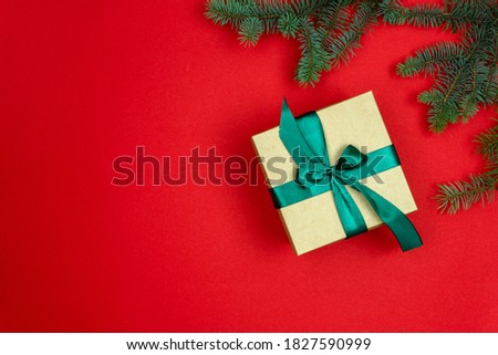 Christmas fir branches on a red background and gift wrap with a green bow. The craft-colored gift is tied with a zedy ribbon. Christmas and New Year theme. Flat lay, top view
