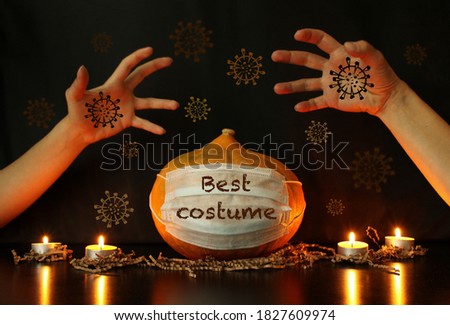 Mother's and child's hands next to Halloween pumpkin in disposable protective mask on the table with burning candles. Black background. Concept of Halloween party during coronavirus pandemic