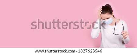 Portrait of a brunette girl with headache in a medical mask and eyeglasses in hand, copy space template, banner.