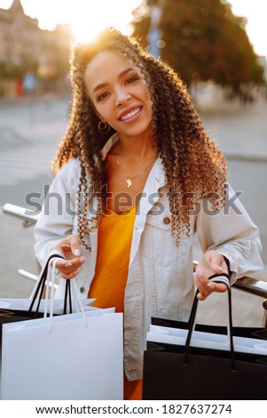 Young woman with shopping bags walking on street. Fashionable african american model carrying shopping bags on road. Purchases, black friday, discounts, sale concept.
