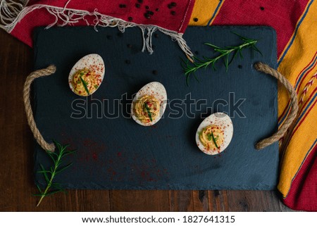 Devil eggs with rosemary and paprika on a table with a cloth and pepper