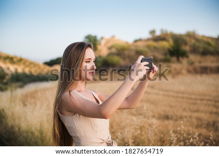 blonde young woman taking photos in the field with her mobile phone