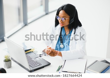 African doctor wear headset consult patient make online webcam video call on laptop screen. Telemedicine videoconference remote computer app virtual meeting. Over shoulder videocall view. Royalty-Free Stock Photo #1827664424