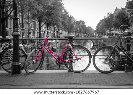 A picture of a pink bike on the bridge over the channel in Amsterdam. The background is black and white. 