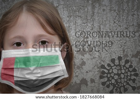 Little girl in medical mask with flag of stands near the old vintage wall with text coronavirus, covid, and virus picture. Stop virus