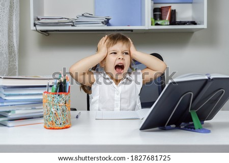 an exhausted little girl grabbed her head and screams while sitting at a table with textbooks. too much homework Royalty-Free Stock Photo #1827681725