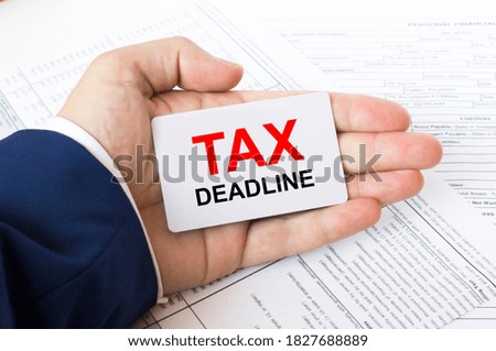 A man's hand is on the financial tables holding a business card with the inscription Tax Deadline. Business concept photo