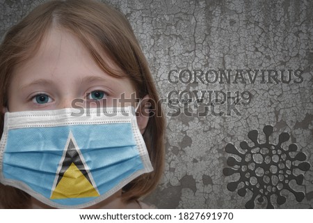 Little girl in medical mask with flag of saint lucia stands near the old vintage wall with text coronavirus, covid, and virus picture. Stop virus