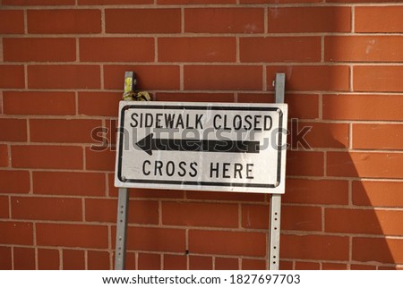 Sign "Sidewalk closed. Cross Here" on a red brick wall background