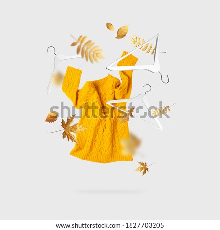 Yellow orange flying women's knitted sweater white wooden hangers golden autumn leaves on gray background. Autumn sale Creative clothing concept trendy fall winter cozy pullover jersey. Female fashion