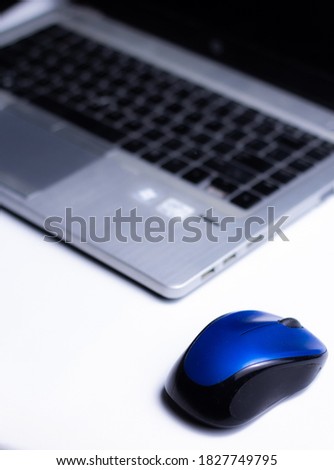 Blue wireless mouse lying with notebook on table in office and ready to be used.