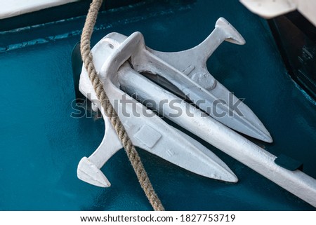 A white anchor lies on a blue background next to a twisted hemp rope