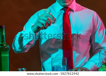 Barman preparing alcoholic drink with a cocktail shaker at the bar with some glasses of liqueur. 