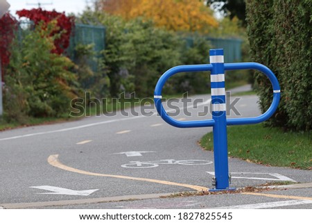 A blue post separating the bike path, trees and cedar hedges
