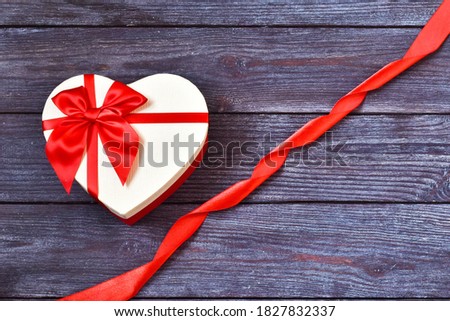 White gift box heart with a red bow, ribbon on a wooden background. Concept of Valentine's Day, anniversary, mother's day and birthday, greeting card.Copy space, top view.