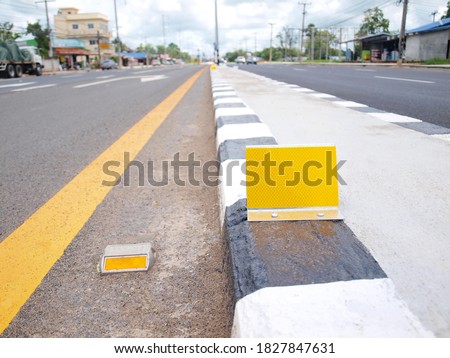 Reflector on median strip. Yellow road markings and concrete curb dividers to increase the safety of traffic on the road. On the background of buildings and blue sky. Selective focus
 Royalty-Free Stock Photo #1827847631