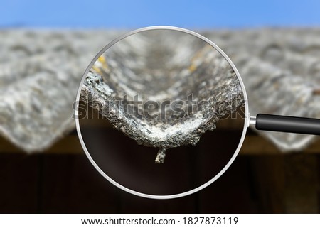 Old and very dangerous asbestos roof. Asbestos dust in the environment. Health problems. View through magnifying glass Royalty-Free Stock Photo #1827873119