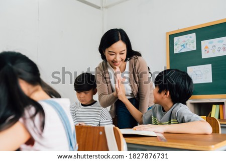 Young Asian teacher giving boy high five in school, success, achievement, happiness. Asia school boy with young woman in class. Royalty-Free Stock Photo #1827876731