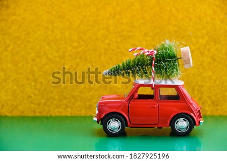 Gift by car. Red toy retro car delivering a gift on a green-yellow background. Postcard for New Year, Christmas. Delivery of gifts.