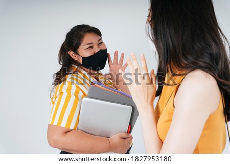 Two asian women wear mask waving hand to say hello to each other.
