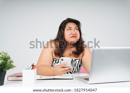 Upset bored asian chubby woman at working desk in office, looking up.