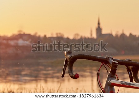 Part of a black red gray racing bike on the river in the yellow orange evening light at sunset in front of the skyline, insects fly through the picture