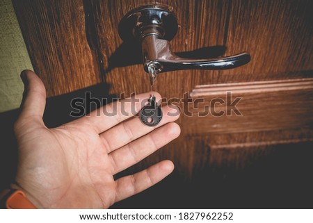 A man holds in his hand a small light broken key against the background of a door lock. Photo in the old style with vignetting.