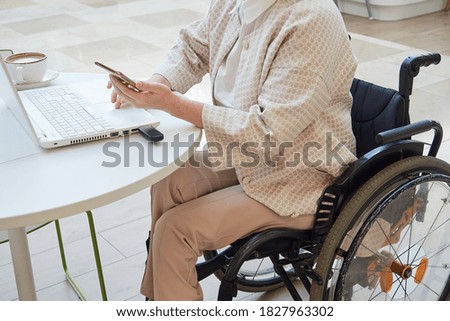 Cropped image of a woman in wheelchair working at a laptop, in the interior of a cafe. Remote work concept, distance learning