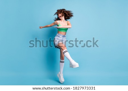 Photo of careless active sportive lady model yell shout hands side raised leg windy hair dancing courses master class advert wear green top jeans skirt isolated pastel blue color background