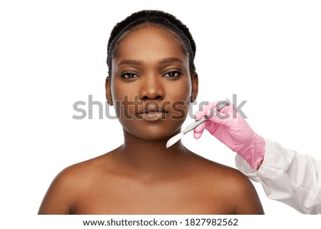 beauty, plastic surgery and people concept - portrait of beautiful young african american woman and hand with scalpel knife over white background