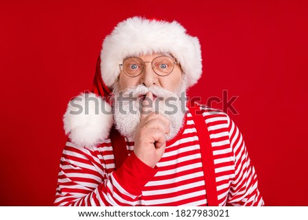 Photo of pensioner old man finger cover lips spotted put gift tell you keep existence secret wear santa costume suspenders spectacles striped shirt headwear isolated red color background