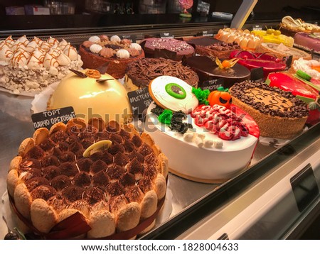 Translation of the inscription on the price tags into Russian: Cake Pancho Walnut, Cake Aristocrat, Cake Chocoholic. Variety of cakes decorated in style of Halloween in the pastry shop window.