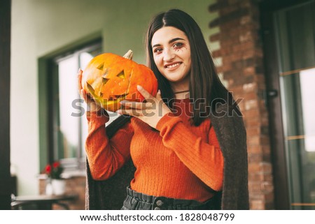 A beautiful girl with dark hair with makeup for the celebration of Halloween holds a pumpkin in her hands and smiles.