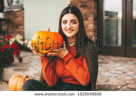 A beautiful girl with dark hair with makeup for the celebration of Halloween holds a pumpkin in her hands and smiles.
