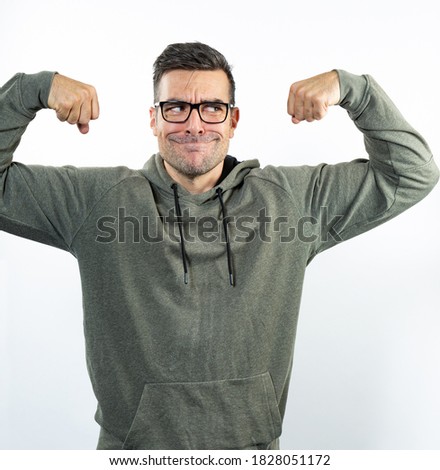 Goofy man wearing casual clothes makes a funny face and flexing arms.