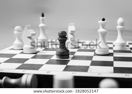 One black pawn stands against a whole board of white chess pieces, selective focus, copy space